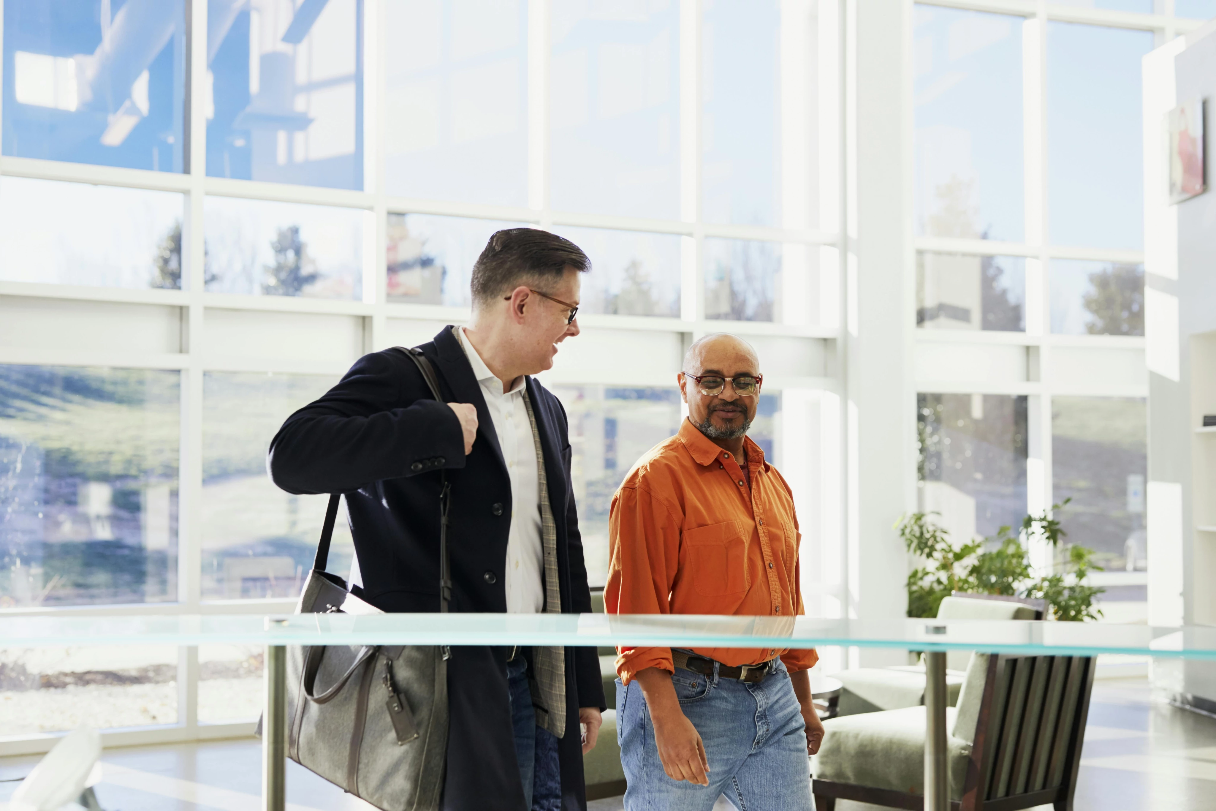 Two men walking in a bright, modern office space, engaged in conversation.