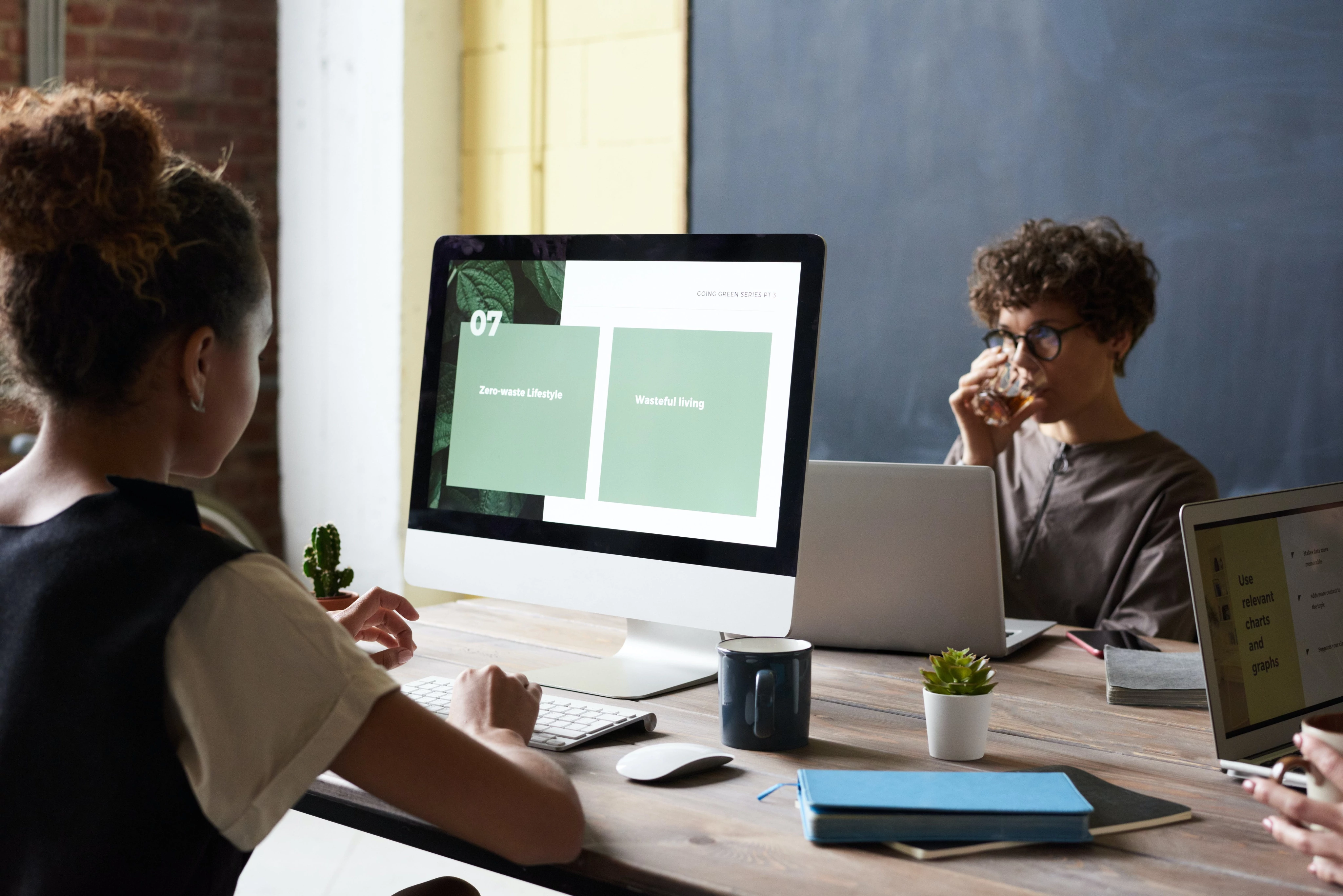 Three people working at a desk with a computer and notebooks.