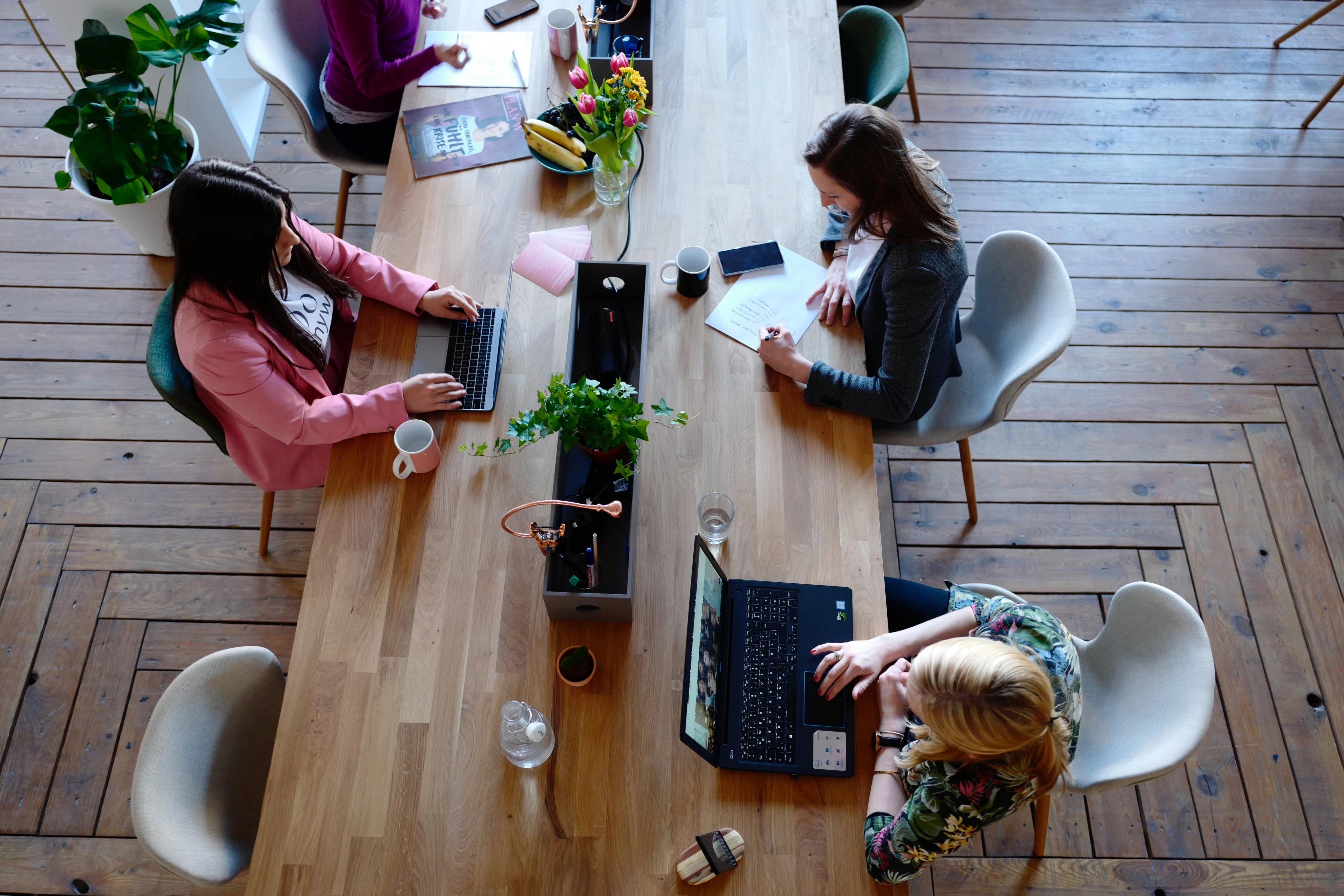 Four people working at a wooden table with laptops and notes.