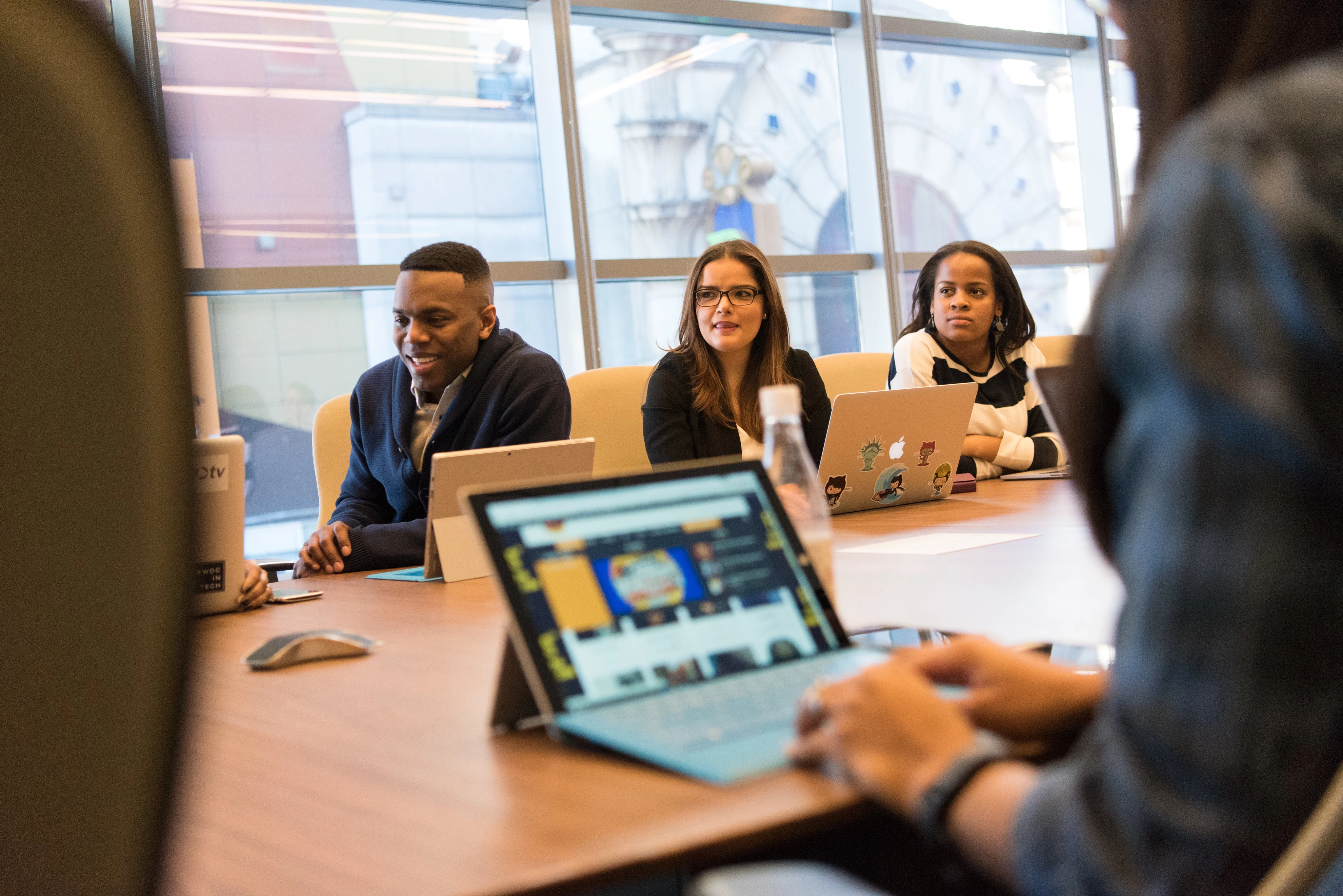 People in a meeting room with laptops, engaged in discussion.