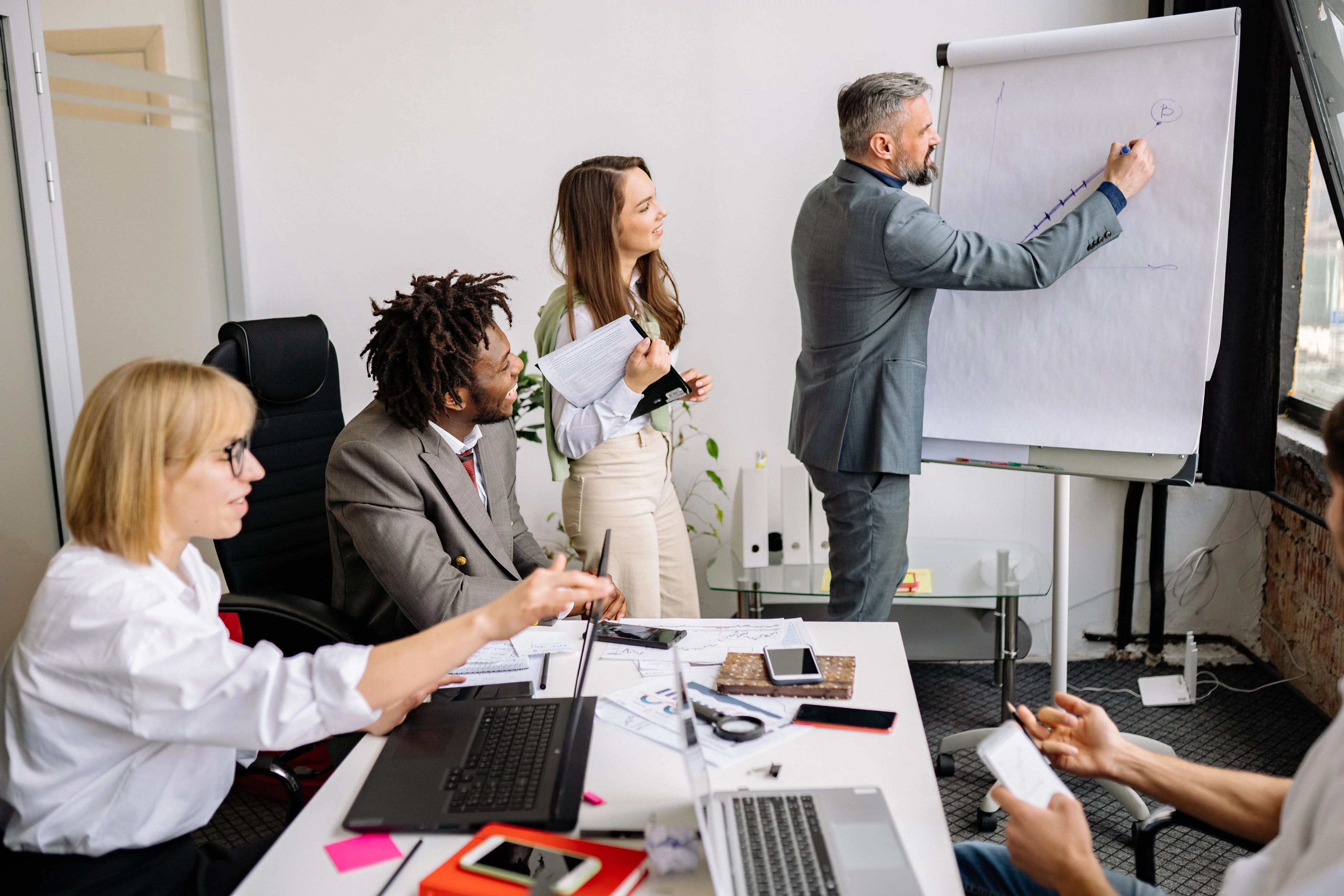 Four people in a meeting, one writing on a flip chart.