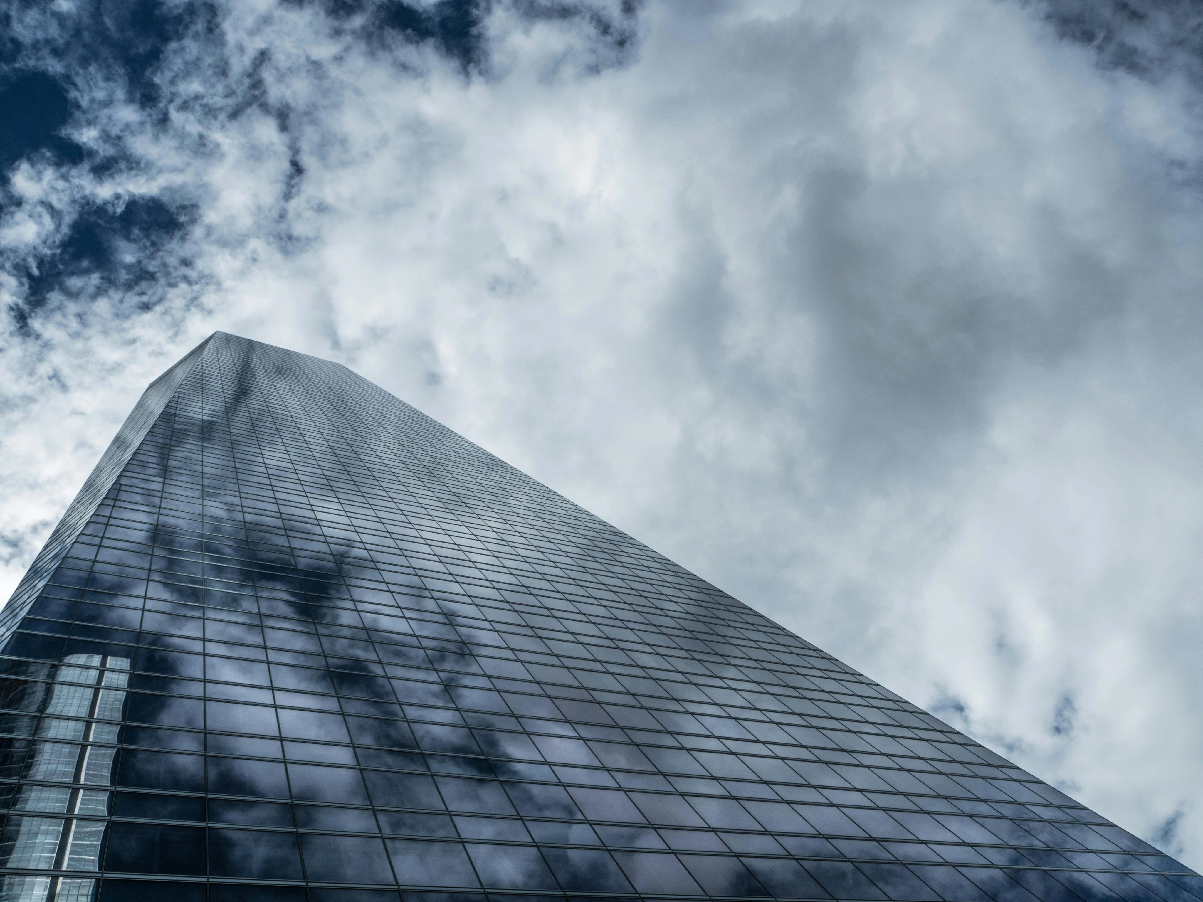 Tall glass skyscraper with cloudy sky reflection.
